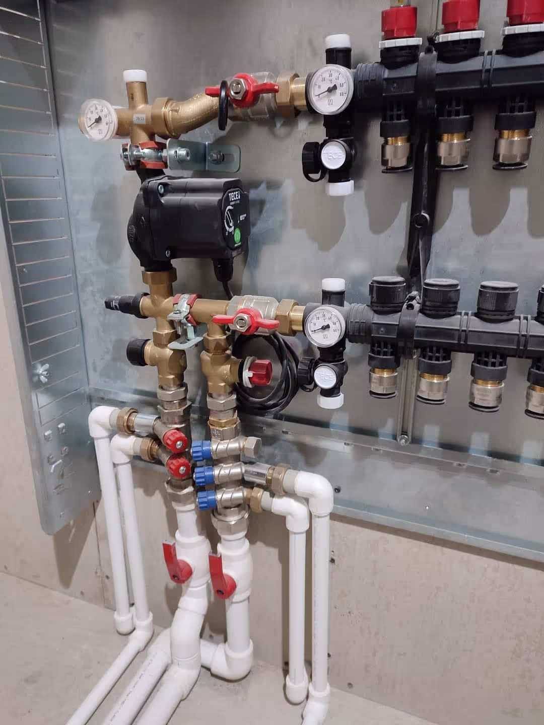 A close-up of a heating manifold system with multiple valves, gauges, and pipes connected to a control panel.