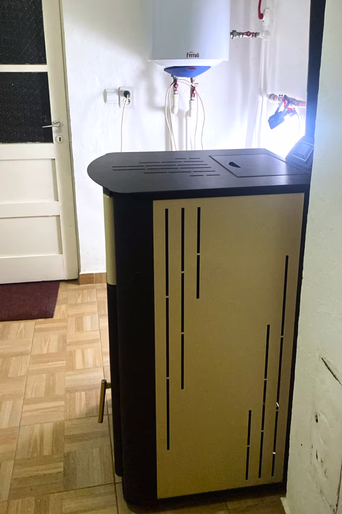Side view of a Ferroli heating stove placed in a room, with a water heater mounted on the wall in the background.