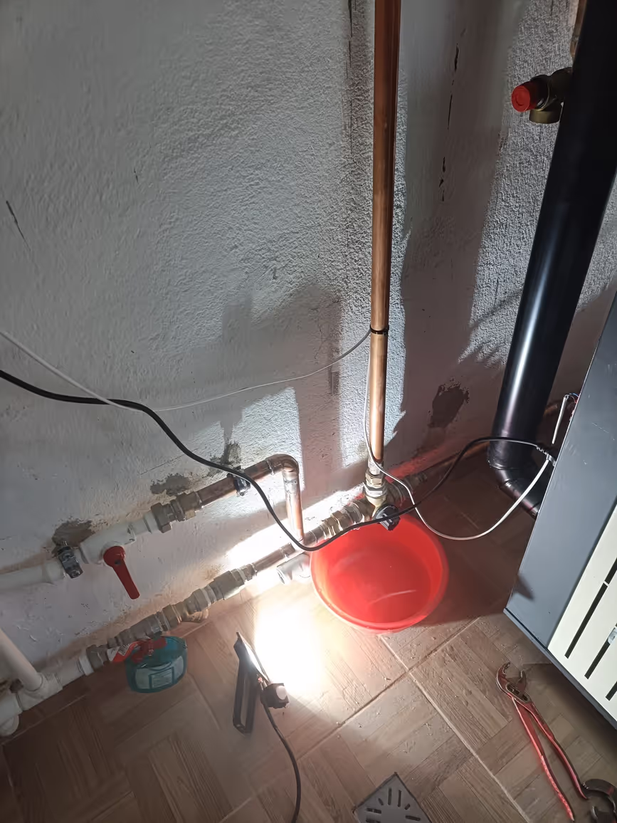Close-up of plumbing pipes with a red bucket placed below a joint to catch any leaks.
