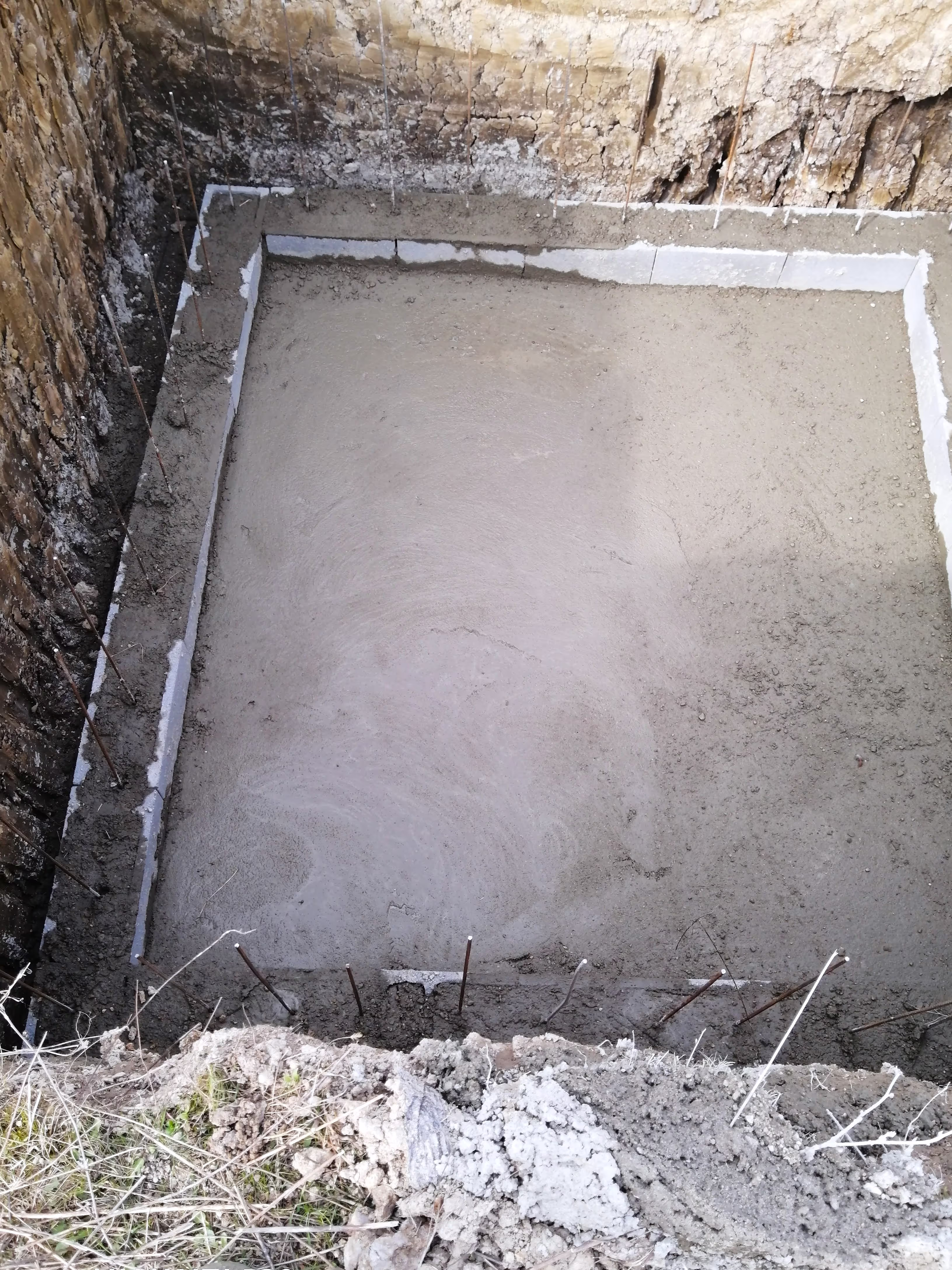 A closer view of the concrete foundation inside the excavation, with metal reinforcement rods protruding from the walls.