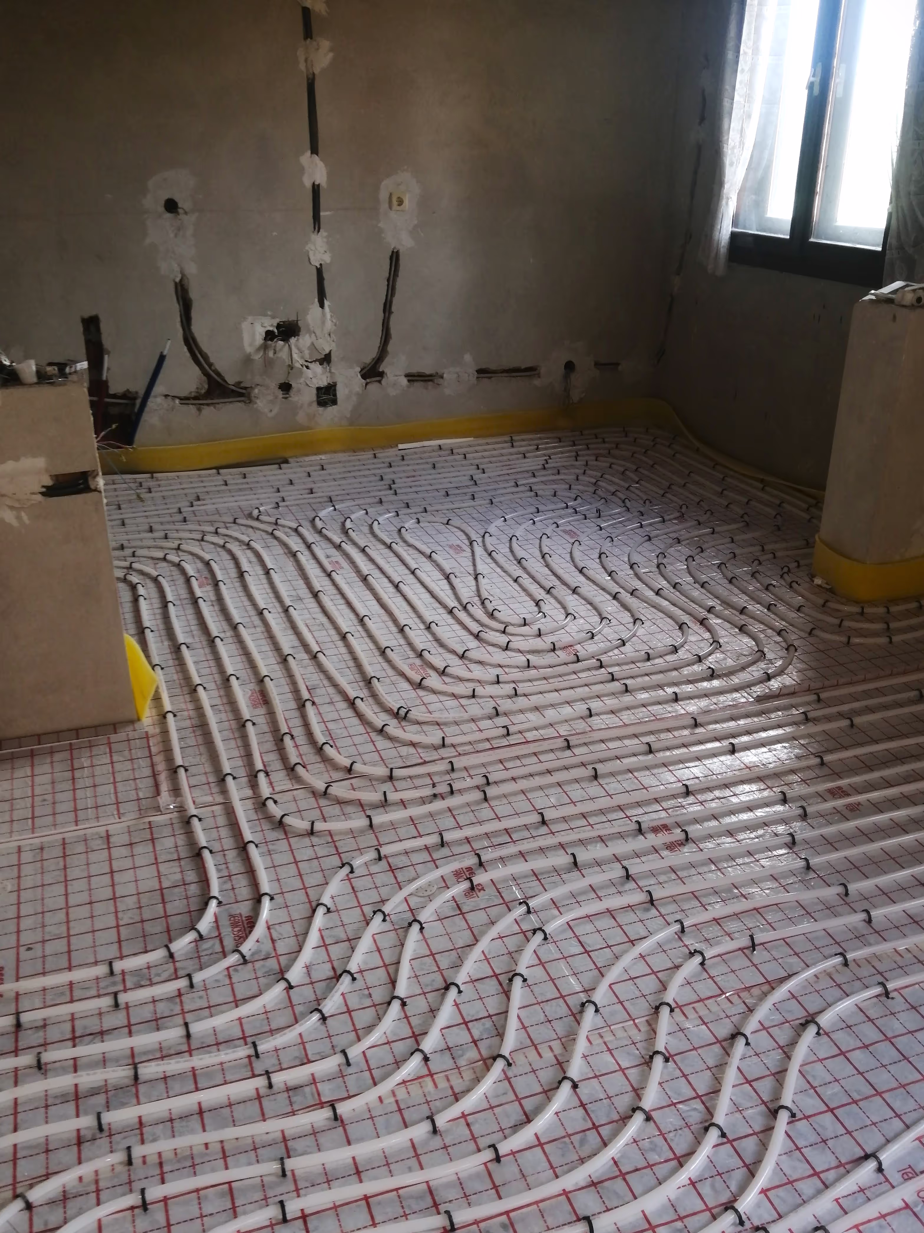 A room under renovation with underfloor heating pipes neatly arranged in a pattern on an insulation grid.