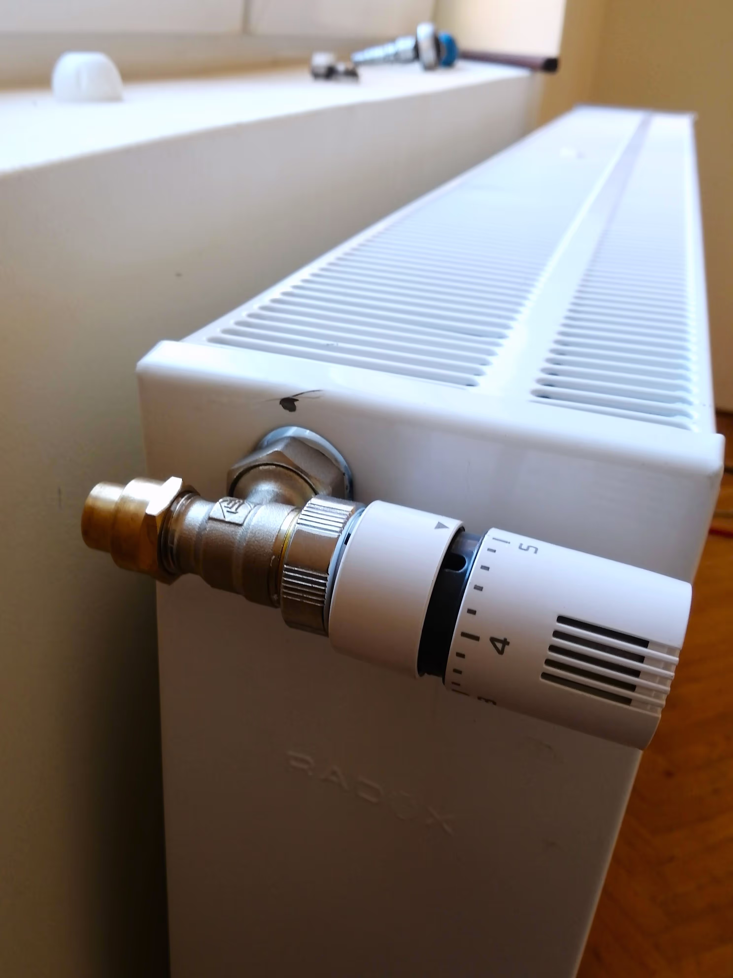 A close-up of a white radiator with a thermostat valve attached, showing numbered temperature settings for controlling heat output.