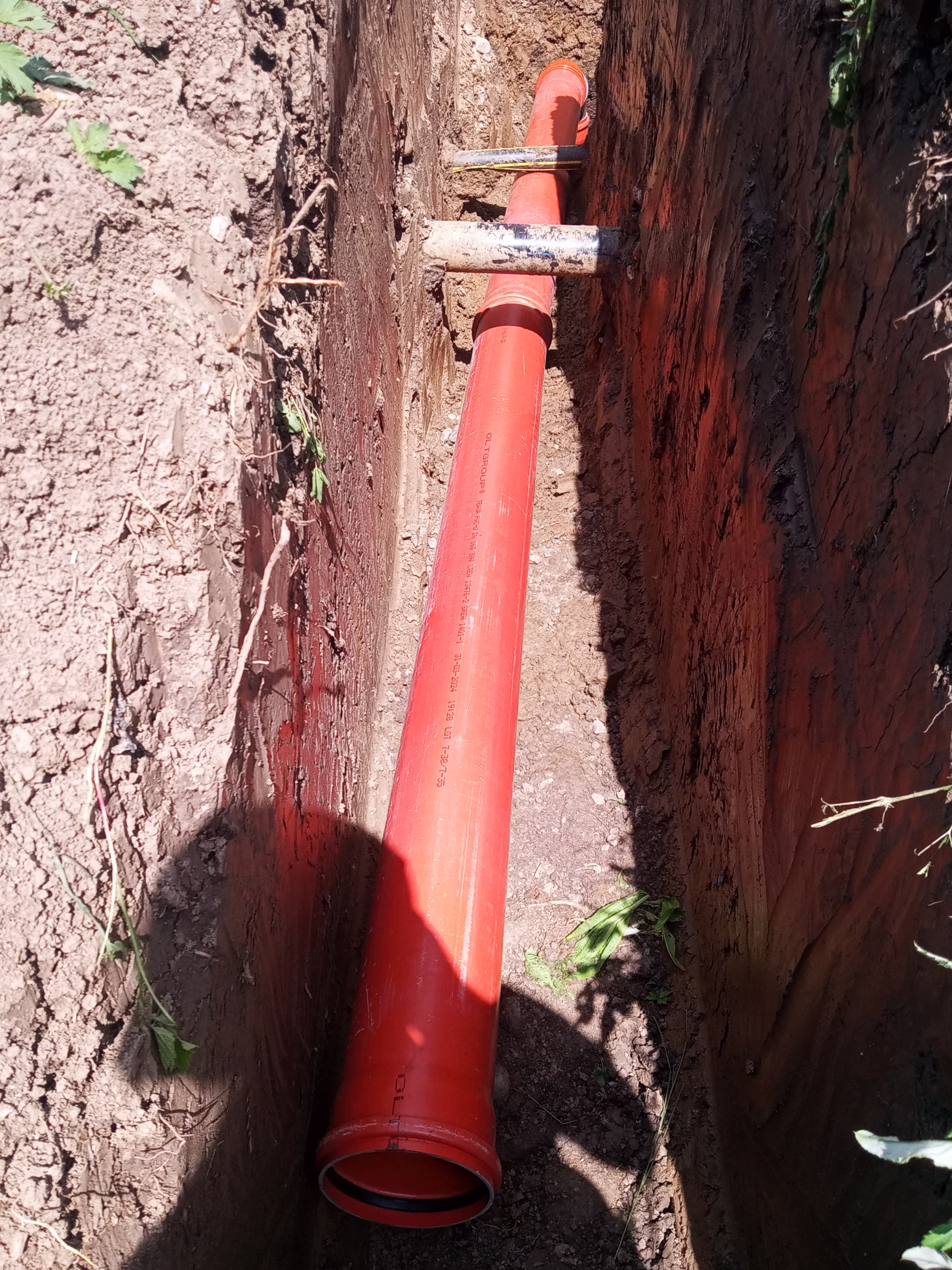 A close-up of a large orange drainage pipe installed in a deep trench, secured by metal supports.