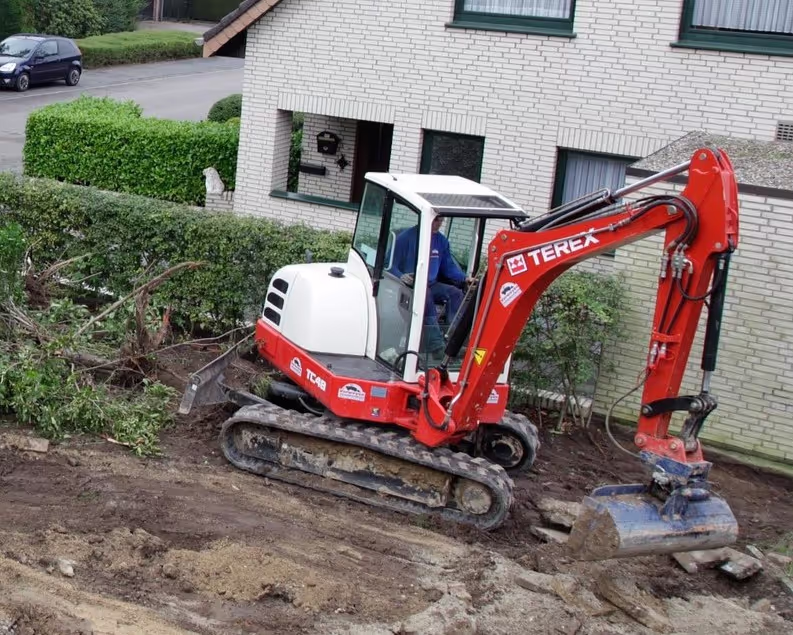 Mini excavator performing earthworks and landscaping near a residential home during construction.